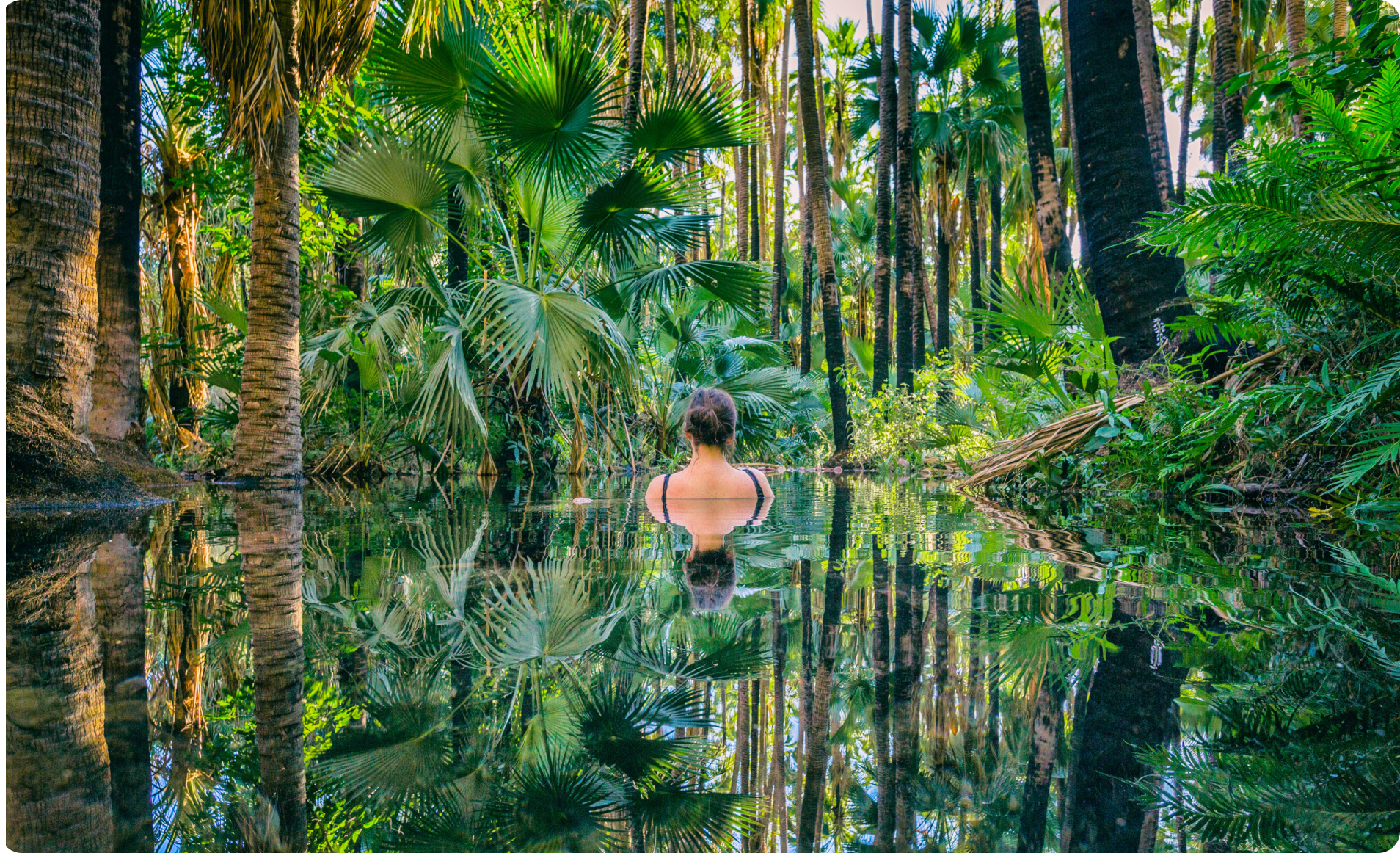 A woman is in a pool surrounded by lush landscaping.