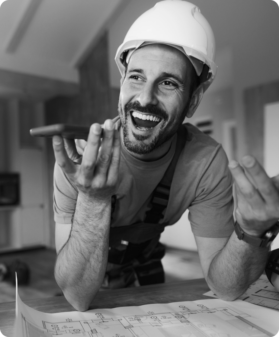 A man in a hard hat talks excitedly into his mobile phone.