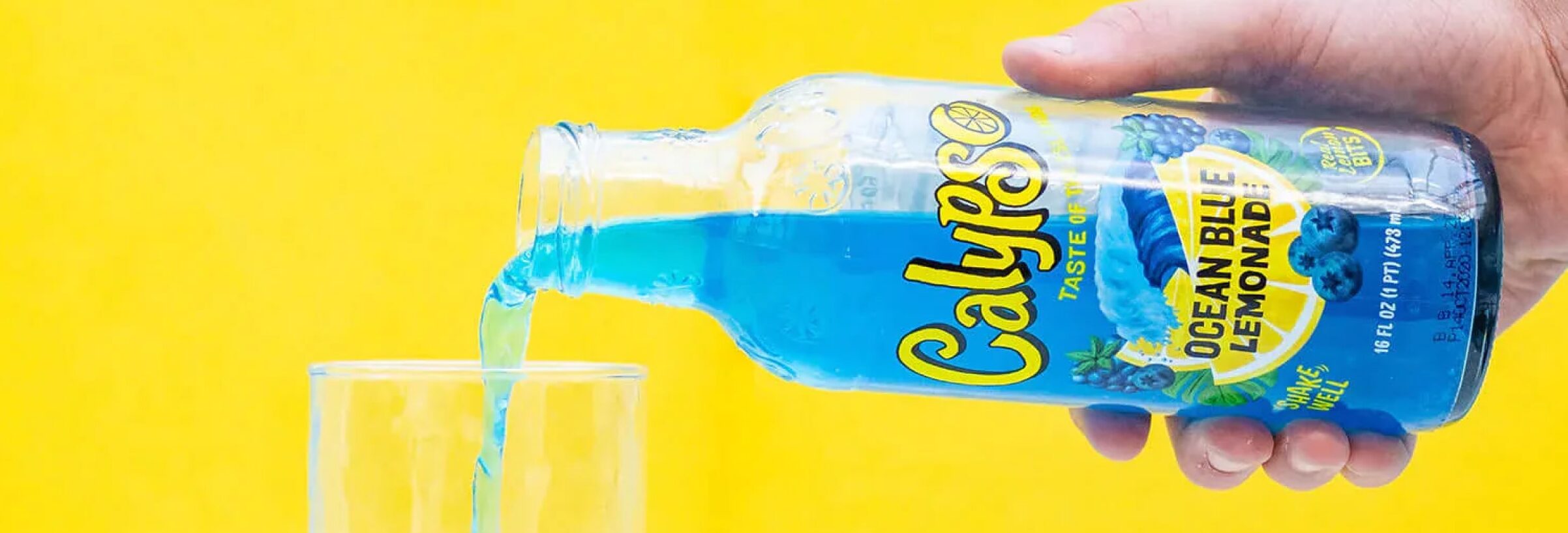 A hand pours lemonade into a glass.