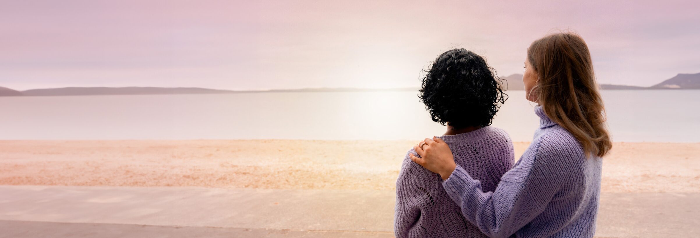 Two woman stand looking out over a bay.