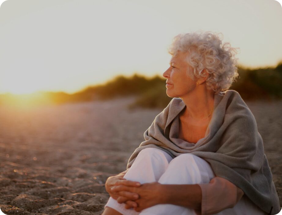 Older woman at the beaching looking at the sunset.